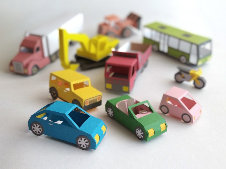 May include: A collection of colorful paper toy vehicles, including a blue car, green convertible, pink car, yellow jeep, red truck, and a yellow excavator. Other vehicles include a bus, motorcycle, and a semi-truck.