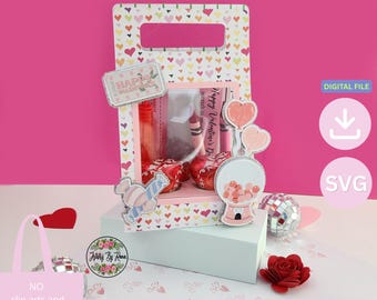 Pode incluir: Um suporte de papel retangular com alça, decorado com um padrão de corações multicoloridos. Possui uma janela central exibindo itens vermelhos, um recorte de máquina de chicletes e um gráfico de doce. O texto inclui "HAPPY VALENTINES".