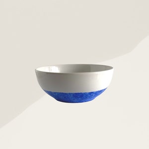Peut inclure: Un bol en céramique blanc avec une bande bleue vive autour de la base. Le bol présente un design simple et moderne, idéal pour servir des aliments ou comme élément décoratif. Le bleu ajoute une touche de couleur.