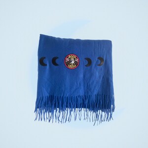 Peut inclure: Une écharpe bleue à franges avec un croissant de lune noir et un patch brodé "Moon Child".