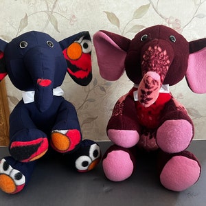 May include: Two plush elephant toys, one blue with red and orange accents and the other maroon with pink accents. Both have white bow ties.