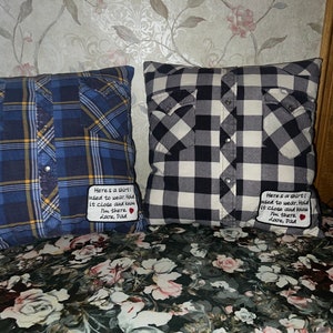 May include: Two decorative pillows made from repurposed plaid shirts. Each pillow has a small embroidered patch with the text "Here's a shirt! I need to wear. Hold it close and know I'm there. Love, Dad".