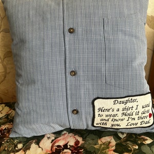 May include: A blue pillow with a pocket and buttons, made to look like a shirt. It has a white embroidered patch with the text "Daughter, Here's a shirt I used to wear. Hold it close and know I'm there with you, Love Dad."