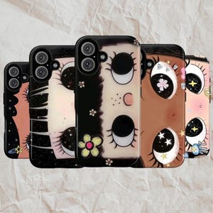 May include: Five phone cases with distinct designs. Each case has a black border and a different illustration, such as eyes, moons, stars, and floral patterns. The colour scheme includes black, white, pink, and brown.