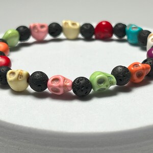 May include: A colorful bracelet with black lava rock beads and skull-shaped beads in various colors, including pink, green, orange, and turquoise.