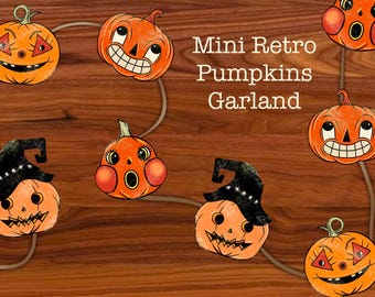 Puede incluir: Una guirnalda de mini calabazas retro con caras sonrientes, algunas con sombreros de bruja. Las calabazas son naranjas con detalles negros y están ensartadas en un cordón marrón claro. Se muestra el texto "Mini Retro Pumpkins Garland".