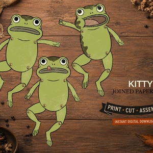 Può includere: Tre bambole di carta a forma di rana verde con arti articolati collegati da rivetti metallici. Il testo recita KITTY JOINED PAPER DOLL, PRINT CUT ASSEMBLE e INSTANT DIGITAL DOWNLOAD. Le rane hanno grandi occhi su una superficie in legno.