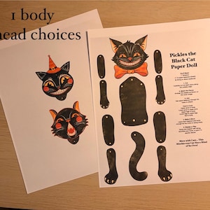 May include: A paper doll craft kit titled Pickles the Black Cat Paper Doll, featuring one black cat body, three interchangeable cat heads with orange accents, and separate limbs. The printed sheets include assembly instructions and text.