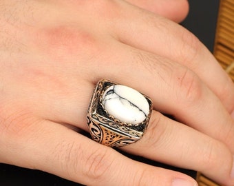 May include: A silver ring with an oval white stone set in a square frame. The frame is decorated with intricate filigree designs.