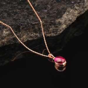 May include: A rose gold chain necklace with a pendant featuring a bright pink oval-shaped gemstone.