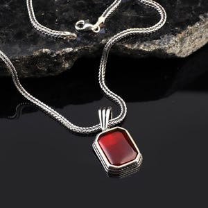 Peut inclure: Un collier en argent avec un pendentif orné d'une pierre précieuse rouge sertie dans un cadre en argent.