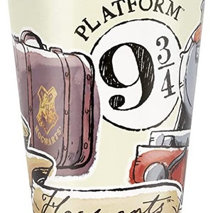 May include: A paper cup with a cream background featuring illustrations of a suitcase, a train, and the words "Platform 9 3/4" and "Hogwarts". The suitcase is brown with a gold crest.