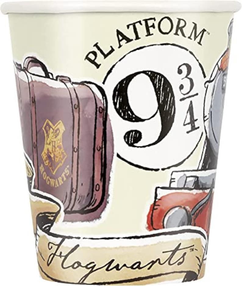 May include: A paper cup with a cream background featuring illustrations of a suitcase, a train, and the words "Platform 9 3/4" and "Hogwarts". The suitcase is brown with a gold crest.
