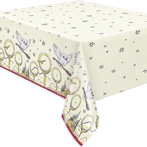 May include: Cream-colored tablecloth with a repeating pattern of stars. The border features owls on broomsticks, golden hoops, and a castle design. A red border frames the design.