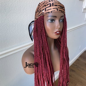 Puede incluir: Una peluca trenzada color burdeos con trenzas largas y rectas. La peluca est&aacute; adornada con una bufanda de sat&eacute;n de color marr&oacute;n y negro con estampado.