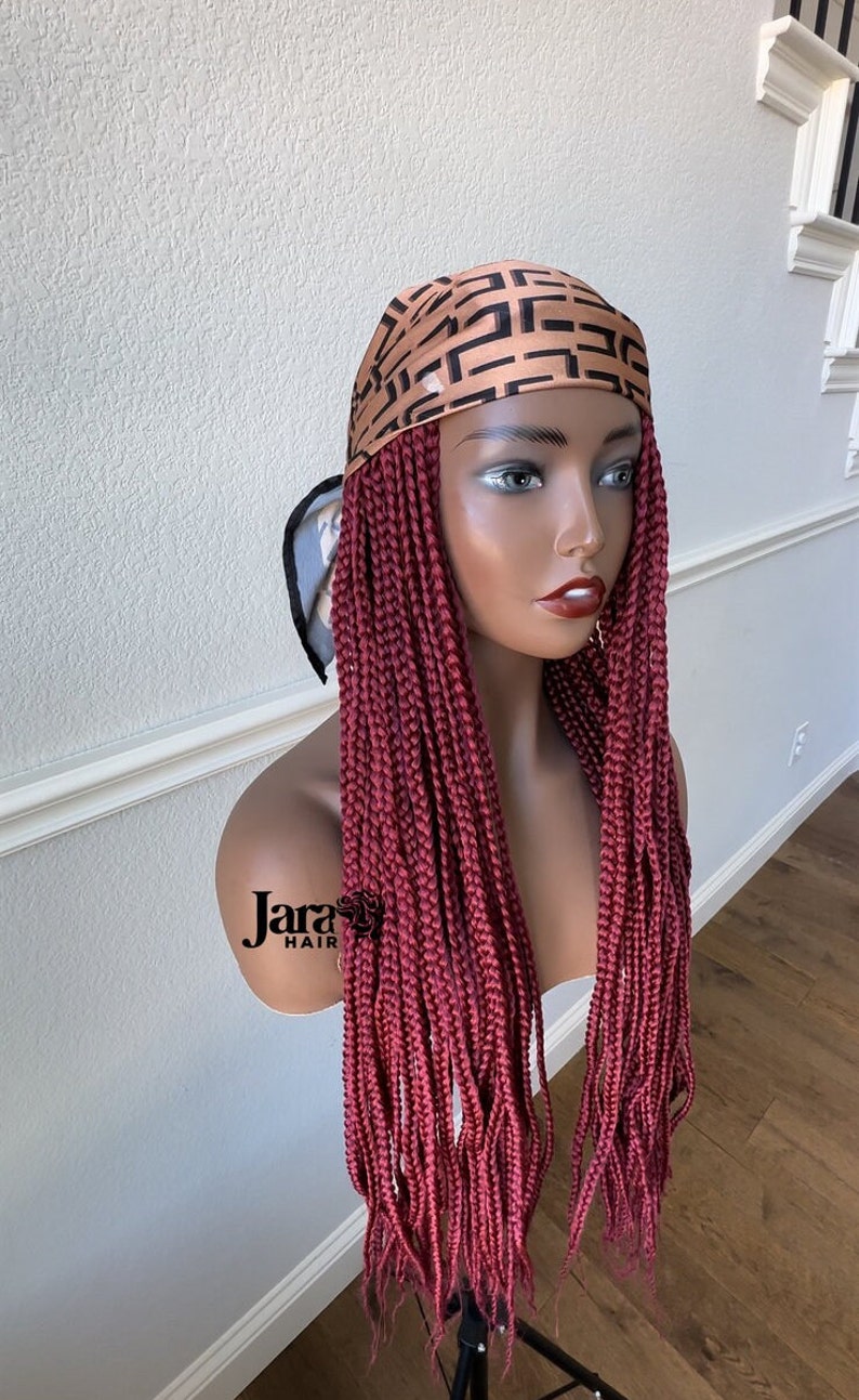 Puede incluir: Una peluca trenzada color burdeos con trenzas largas y rectas. La peluca est&aacute; adornada con una bufanda de sat&eacute;n de color marr&oacute;n y negro con estampado.