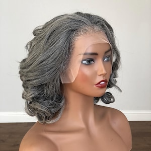 K&ouml;nnte beinhalten: Ein Schaufensterpuppenkopf mit einer kurzen, gewellten Per&uuml;cke in Grau- und Silbert&ouml;nen. Die Per&uuml;cke hat eine Spitze vorne f&uuml;r einen nat&uuml;rlichen Look. Die Schaufensterpuppe hat bemalte Gesichtsz&uuml;ge, darunter roter Lippenstift und dunkle Augenbrauen.