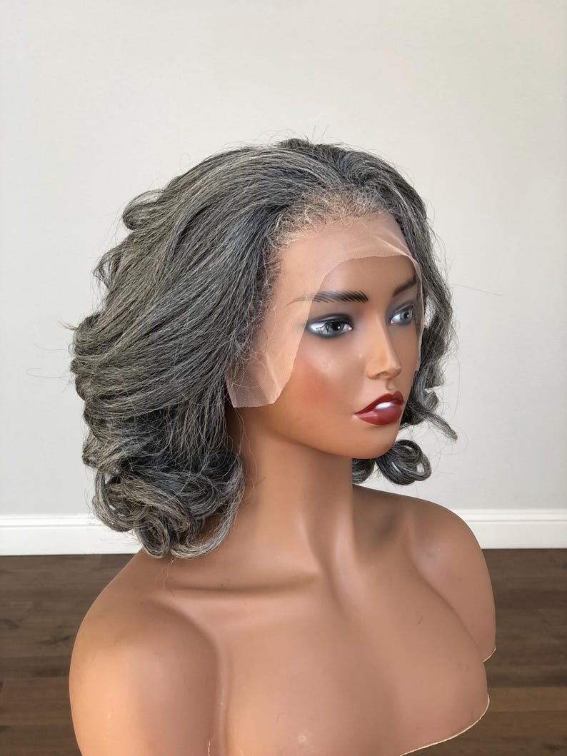 K&ouml;nnte beinhalten: Ein Schaufensterpuppenkopf mit einer kurzen, gewellten Per&uuml;cke in Grau- und Silbert&ouml;nen. Die Per&uuml;cke hat eine Spitze vorne f&uuml;r einen nat&uuml;rlichen Look. Die Schaufensterpuppe hat bemalte Gesichtsz&uuml;ge, darunter roter Lippenstift und dunkle Augenbrauen.