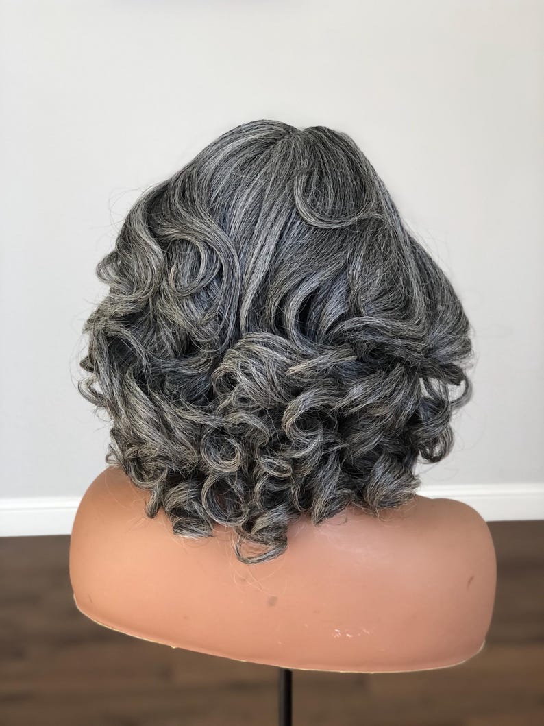 K&ouml;nnte beinhalten: Eine graue Per&uuml;cke mit volumin&ouml;sem, eng gelocktem Haar. Die Per&uuml;cke ist in einer kurzen, abgerundeten Form gestylt, wobei die Locken das Gesicht umrahmen. Die Per&uuml;cke wird auf einem Schaufensterpuppenkopf pr&auml;sentiert.