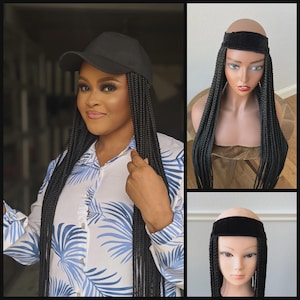 Pode incluir: Boné preto com cabelo trançado preto preso. A imagem também mostra uma cabeça de manequim com o mesmo estilo de cabelo trançado. As tranças são longas e penduradas.