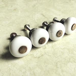 May include: A white ceramic mug with a black handle and the text "But First, Coffee" in a black, bold font. The mug is sitting on a wooden surface. The mug is 4 inches tall.