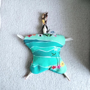 May include: A handmade doll with a turquoise and white tropical print dress. The doll has white arms and legs, a black head, and a small brown figurine on top. The dress features palm trees and flowers.