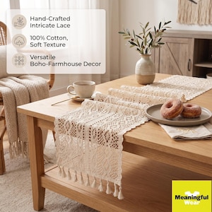 May include: A cream-colored lace table runner with an intricate woven pattern and fringe trim on the ends. The runner is draped over a wooden table, featuring text that highlights hand-crafted lace, 100% cotton material, and decor versatility.