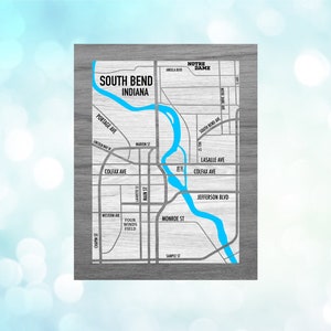 May include: A map of South Bend, Indiana, with a blue river running through it. The map is on a wood-grain background. The text "South Bend, Indiana" is at the top of the map. The text "Notre Dame" is at the top right of the map.
