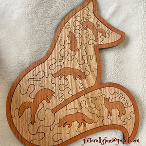 May include: A wooden jigsaw puzzle shaped like a fox with a detailed, intricate design. The puzzle features five foxes in various poses, all cut out from the wood. The puzzle is made of light and dark wood, creating a natural wood grain pattern.