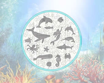 May include: A circular wooden jigsaw puzzle with a blue border, featuring various sea creatures including a whale, dolphin, mermaid, octopus, starfish, seahorse, and crab. The puzzle pieces are cut in a whimsical, intricate design.