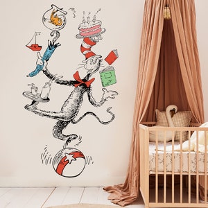 May include: A black and white illustration of the Cat in the Hat balancing a birthday cake, a fishbowl, an umbrella, a tray with a glass and a bottle, and a book on a red and white ball. The illustration is on a white wall with a light brown canopy bed and a white crib in the background.