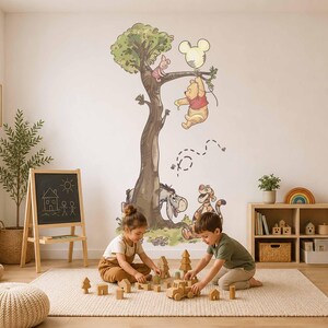 May include: A wall decal featuring a large tree with Winnie the Pooh hanging from a branch by a Mickey Mouse-shaped balloon, Piglet sitting on a branch, and Eeyore and Tigger resting at the base of the tree trunk, all rendered in a soft illustration style.