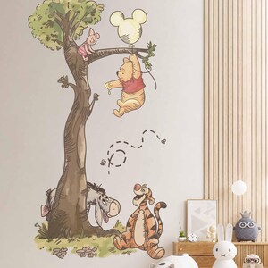 May include: A wall decal featuring Winnie the Pooh hanging from a tree branch while holding a Mickey Mouse-shaped balloon, with Piglet sitting on a branch above, and Eeyore and Tigger standing at the base of the tree with small bees flying nearby.