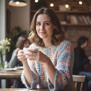 Peut inclure: Une femme dans un café, tenant une tasse de café blanche. Elle porte un pull ajouré pastel bleu, rose et pêche. Le café a une atmosphère chaleureuse et accueillante avec de la lumière naturelle et des tables en bois.
