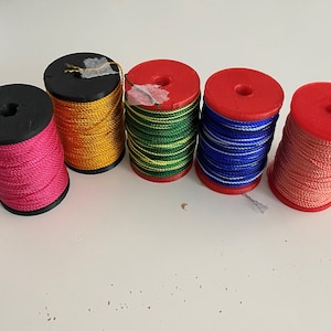 May include: Five spools of thread in different colors. The spools are red, black, gold, green, and pink. The thread is wound around the spools.