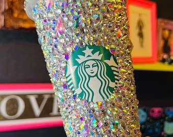 May include: A clear plastic tumbler covered in iridescent rhinestones with a green Starbucks logo featuring a mermaid.