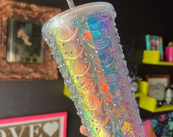 May include: A clear plastic tumbler with a mermaid scale design and iridescent finish. The tumbler has a straw and is perfect for holding cold beverages.