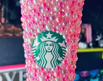 Op de afbeelding: Een roze en witte herbruikbare beker met een Starbucks-logo bedekt met roze en witte parels.