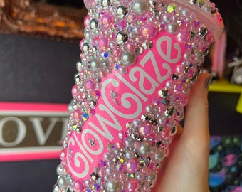 Op de afbeelding: Roze herbruikbare beker met een wit "Glowgaze" logo en bedekt met roze en witte parels en strass.
