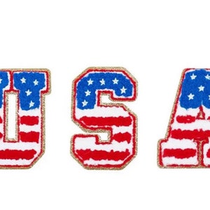 May include: Three embroidered patches spelling "USA". Each letter is designed with the American flag: red and white stripes, blue field with white stars, and a gold glitter border. The patches are on a white background.