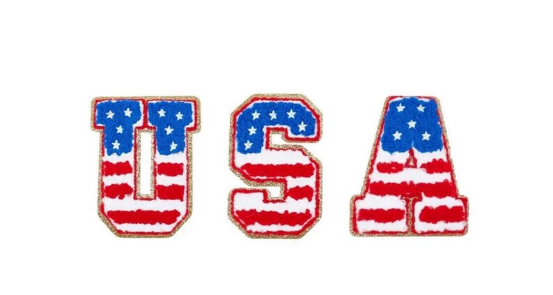 May include: Three embroidered patches spelling "USA". Each letter is designed with the American flag: red and white stripes, blue field with white stars, and a gold glitter border. The patches are on a white background.