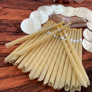 May include: A close-up of a group of beige ear candles with silver bands. The candles are arranged in a fan shape on a wooden surface.