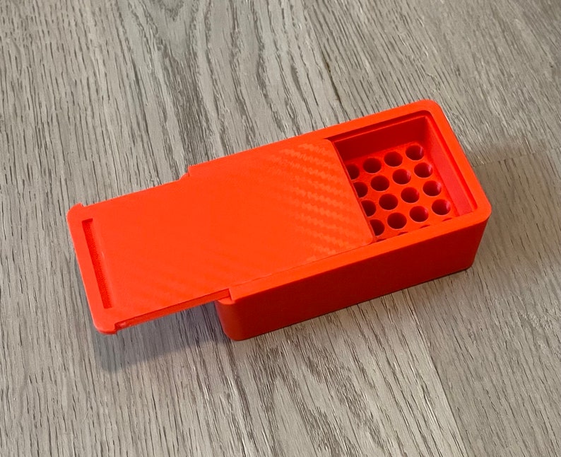 Peut inclure: Une bo&icirc;te en plastique orange vif avec un couvercle &agrave; charni&egrave;re et une grille de trous ronds &agrave; l'int&eacute;rieur. La bo&icirc;te est con&ccedil;ue pour contenir de petits objets, tels que des balles ou des perles.