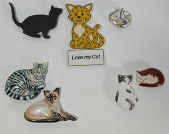 May include: A collection of seven cat-themed decorative items, including a black silhouette of a cat, a yellow and brown cartoon cat with the text "Love my Cat", a striped gray and white cat, a white and gray cat, a brown and white cat, a white cat with gray spots, and a round glass button with a cat design.
