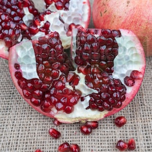 Könnte beinhalten: Nahaufnahme einer aufgeschnittenen Granatapfel, die die leuchtend roten Kerne enthüllt. Der Granatapfel liegt auf einer Jutestoff-Oberfläche.
