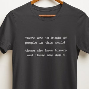 May include: A dark gray t-shirt with white text that reads "There are 10 kinds of people in this world: those who know binary and those who don't."