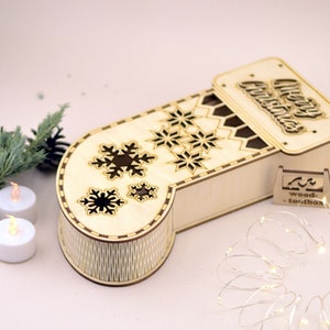 May include: A wooden Christmas stocking box with a cutout design of snowflakes and the words "Merry Christmas". The box is open and has a small wooden tag that says "wood-toolbox".