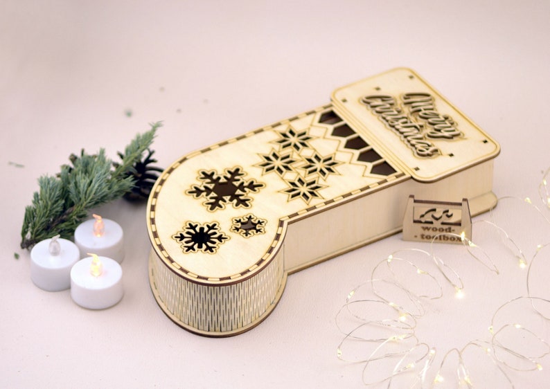 May include: A wooden Christmas stocking box with a cutout design of snowflakes and the words "Merry Christmas". The box is open and has a small wooden tag that says "wood-toolbox".