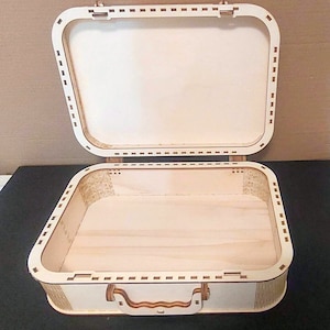 May include: A wooden box shaped like a suitcase with a hinged lid and a handle. The box is made of light brown wood and has a natural finish.