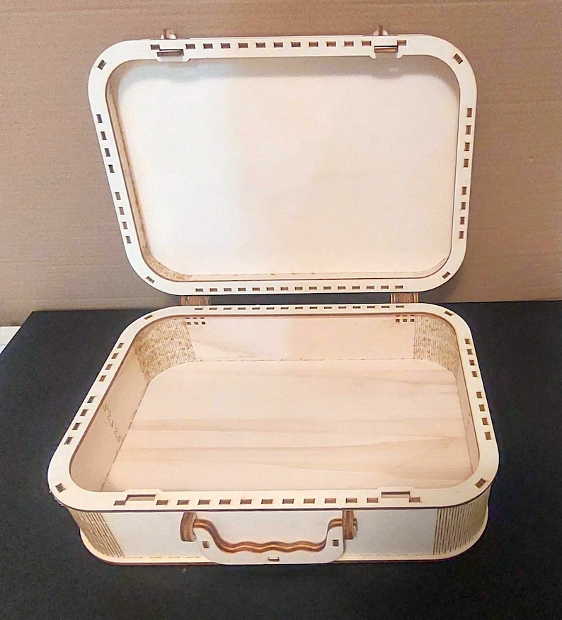May include: A wooden box shaped like a suitcase with a hinged lid and a handle. The box is made of light brown wood and has a natural finish.